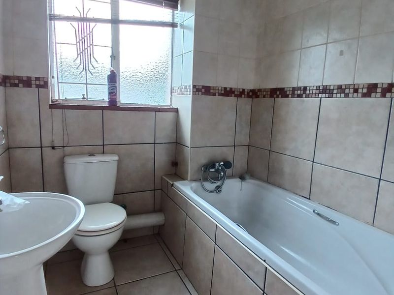 A functional bathroom featuring a pedestal basin, toilet, and bathtub with neutral wall and floor tiling.