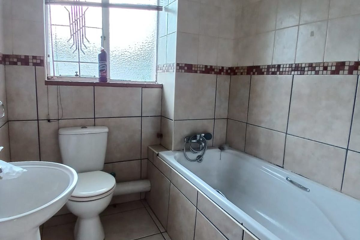 A functional bathroom featuring a pedestal basin, toilet, and bathtub with neutral wall and floor tiling.