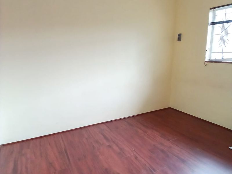 An empty bedroom featuring laminate flooring and a window fitted with security bars.