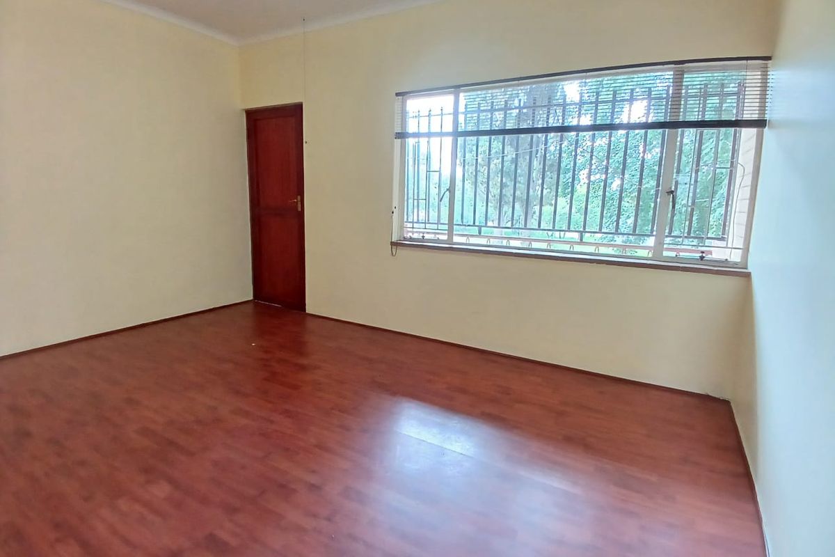 A vacant bedroom featuring laminate flooring, a timber door, and large windows fitted with security bars and blinds.