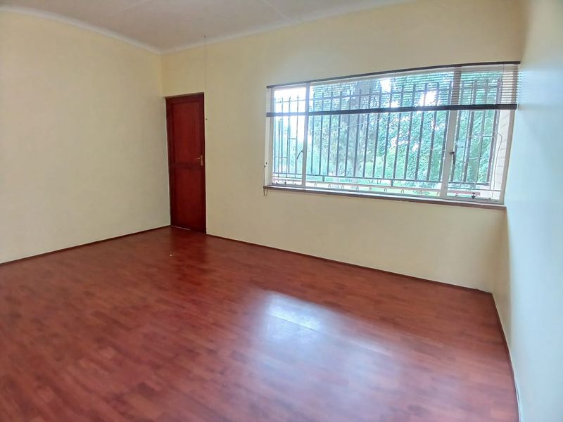 A vacant bedroom featuring laminate flooring, a timber door, and large windows fitted with security bars and blinds.