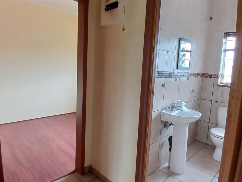 A view from the hallway looking into an adjacent bedroom and a tiled bathroom featuring a pedestal basin and toilet.