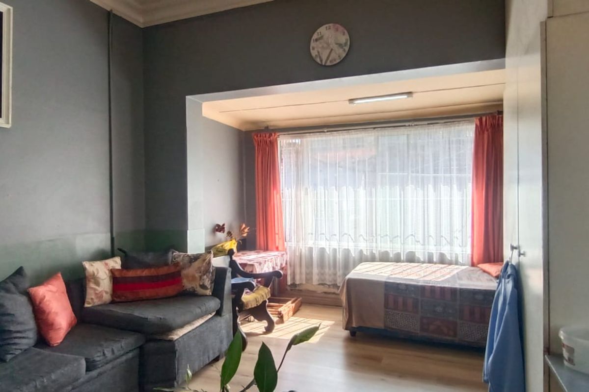 A living room area featuring laminate flooring, built-in storage cupboards, and a large window allowing natural light into the space.