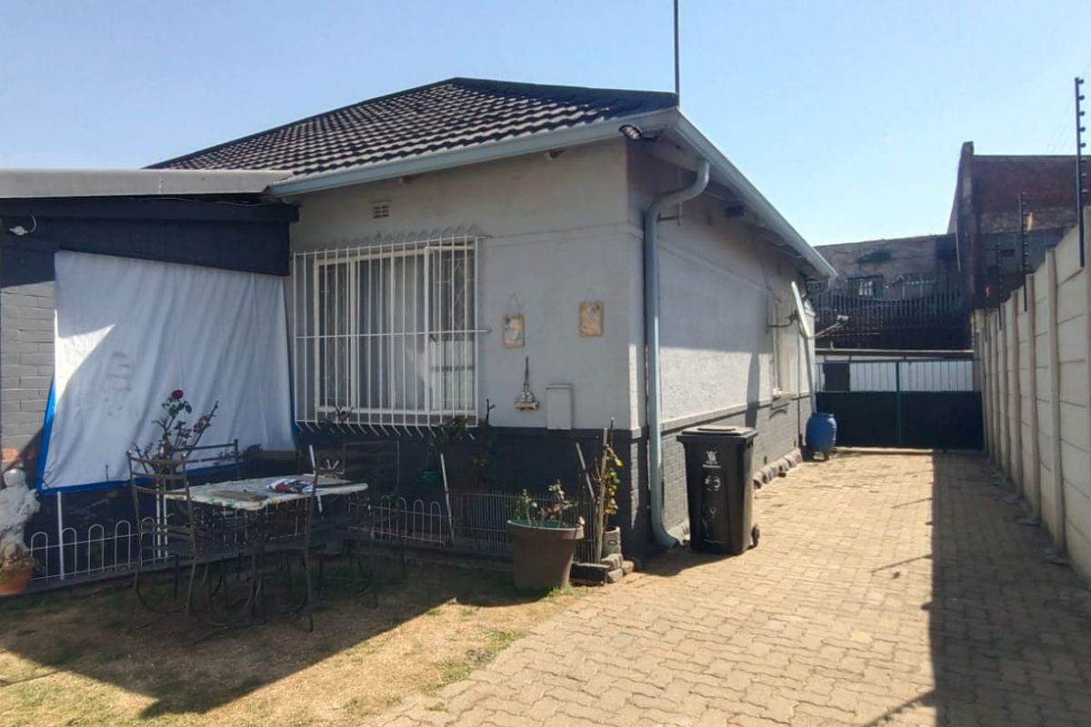 Rear view of the house featuring a covered patio, paved driveway, and secure boundary wall with electric fencing.