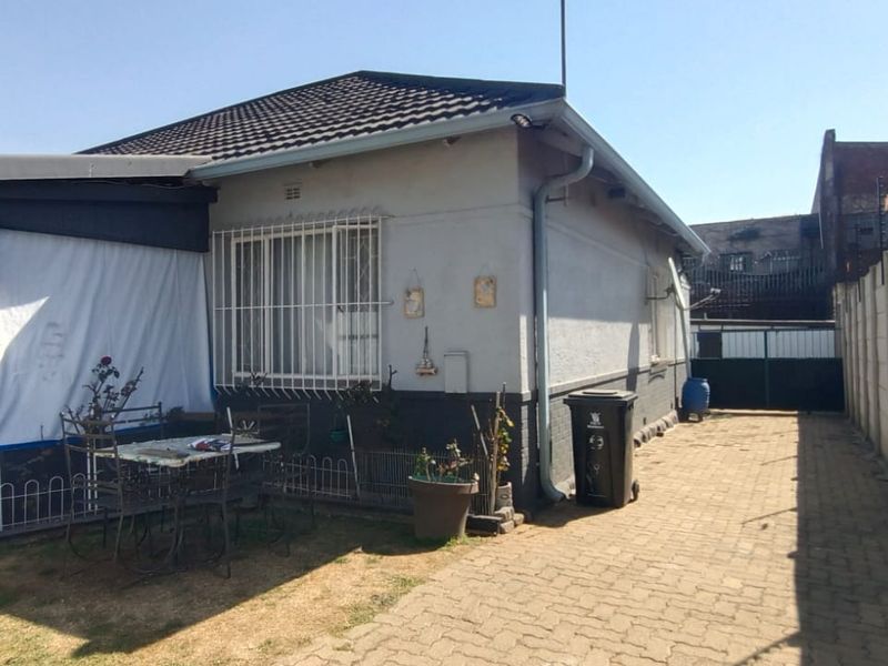 Rear view of the house featuring a covered patio, paved driveway, and secure boundary wall with electric fencing.