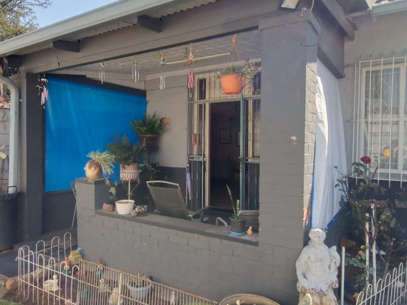 A covered patio area featuring brick masonry and security bars, providing an outdoor transition space to the main entrance of the house.