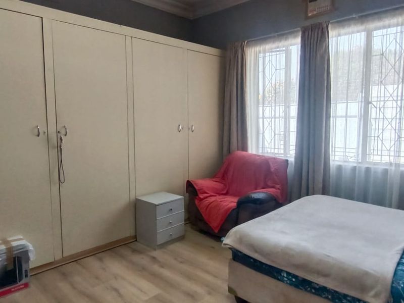 A bedroom featuring extensive built-in cupboards, laminate flooring, and large windows with security bars, offering a functional and well-lit living space.