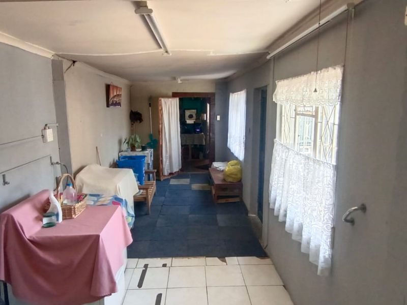 A functional utility or transition space featuring tiled flooring and security window bars, offering potential for renovation or improved storage utility.