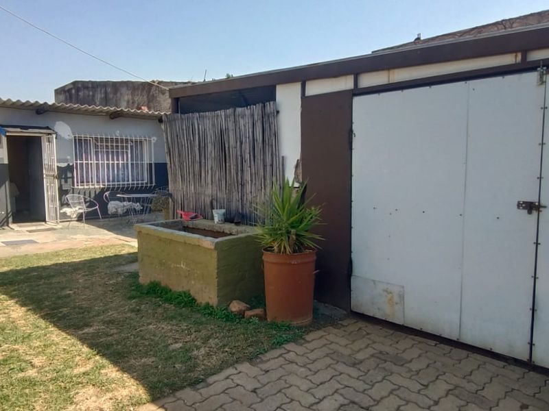 Rear exterior view showing a garage with a paved driveway, security bars on windows, and a small garden area with a brick planter.