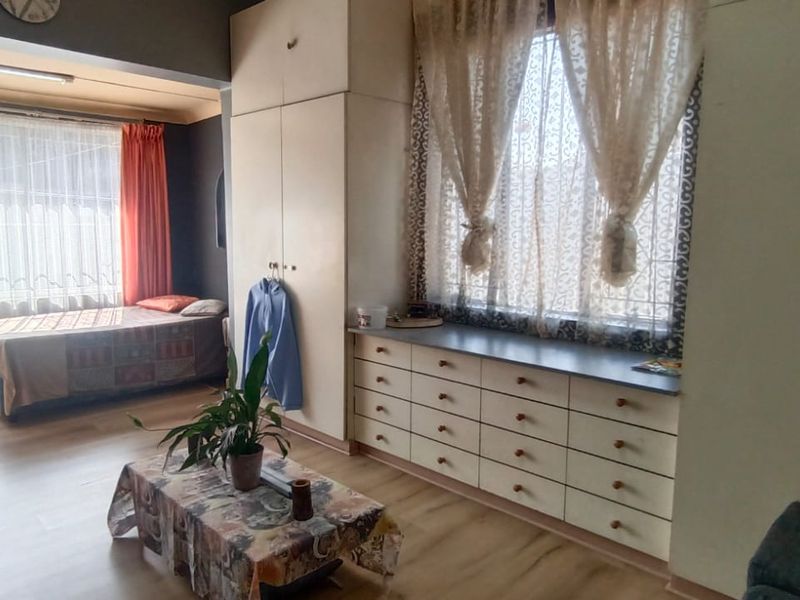 Spacious bedroom featuring extensive built-in cabinetry, laminate flooring, and large windows with security bars, offering a functional layout with potential for modernization.