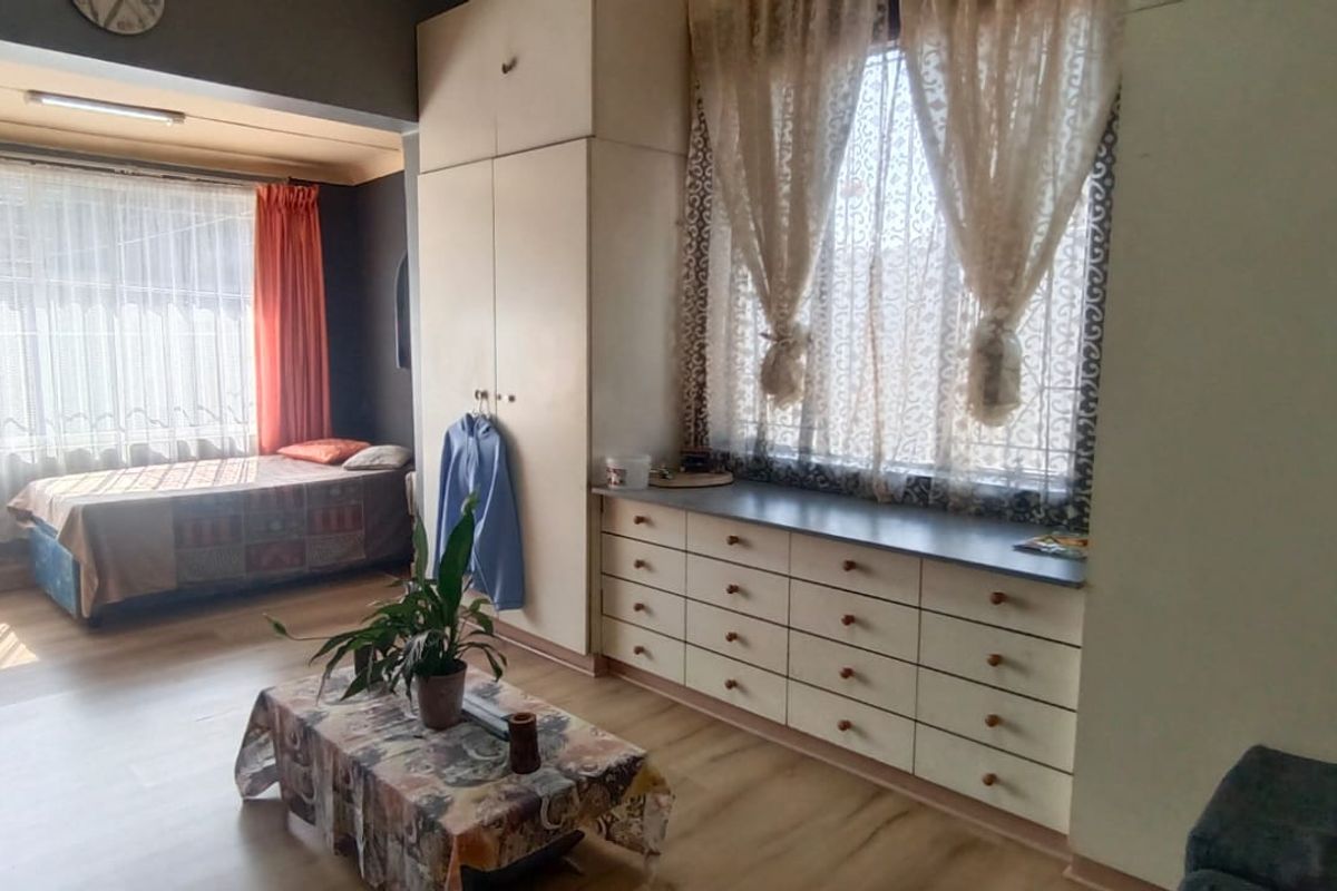 Spacious bedroom featuring extensive built-in cabinetry, laminate flooring, and large windows with security bars, offering a functional layout with potential for modernization.