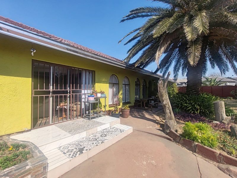 Rear exterior view of the house featuring a tiled patio entrance, arched windows, and a paved walkway leading through the garden.