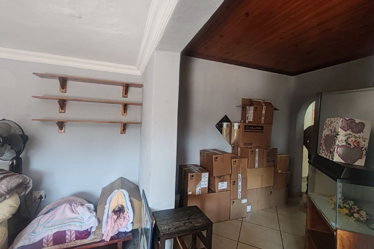 Living area featuring a timber ceiling, crown molding, and ceramic floor tiles, with wall-mounted shelving and an arched doorway leading to adjacent spaces.