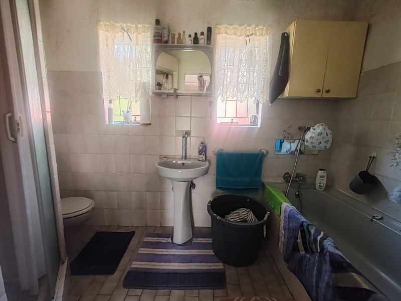 A dated bathroom featuring a pedestal basin, built-in bathtub, and wall-mounted toilet, with tiled finishes throughout. The space requires cosmetic updates and modernization.