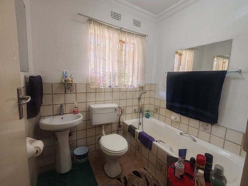 A dated bathroom featuring a pedestal basin, standard toilet, and bathtub with tiled splashbacks, offering potential for modernization and renovation.
