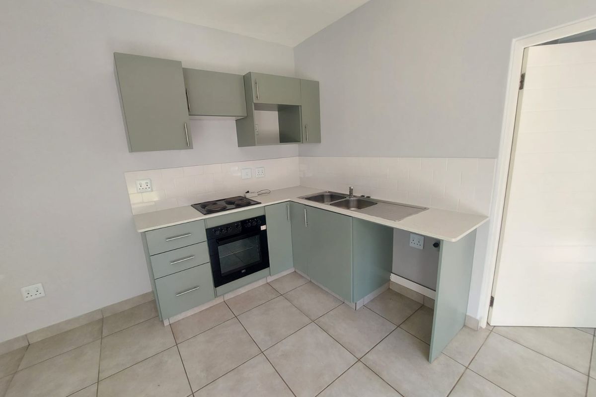 A clean, modern kitchen featuring sage green cabinetry, a built-in oven and hob, stainless steel sink, and neutral tiled flooring.