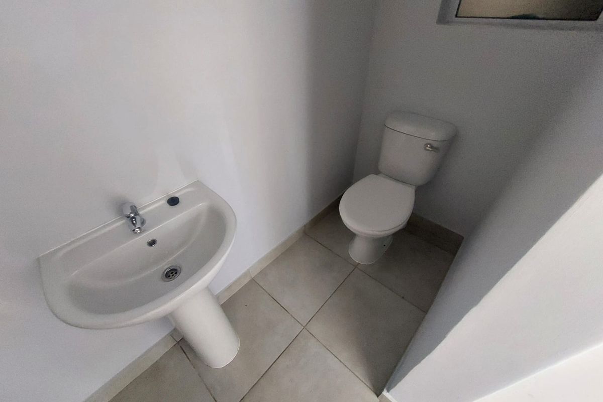 A compact guest bathroom featuring a white pedestal basin and a standard toilet with neutral floor tiling.