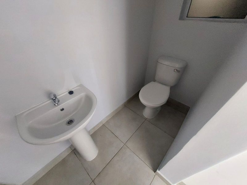 A compact guest bathroom featuring a white pedestal basin and a standard toilet with neutral floor tiling.