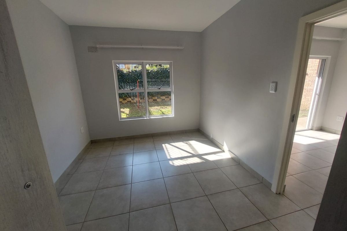 A bright, empty bedroom featuring neutral tiled flooring and a window overlooking the garden area.