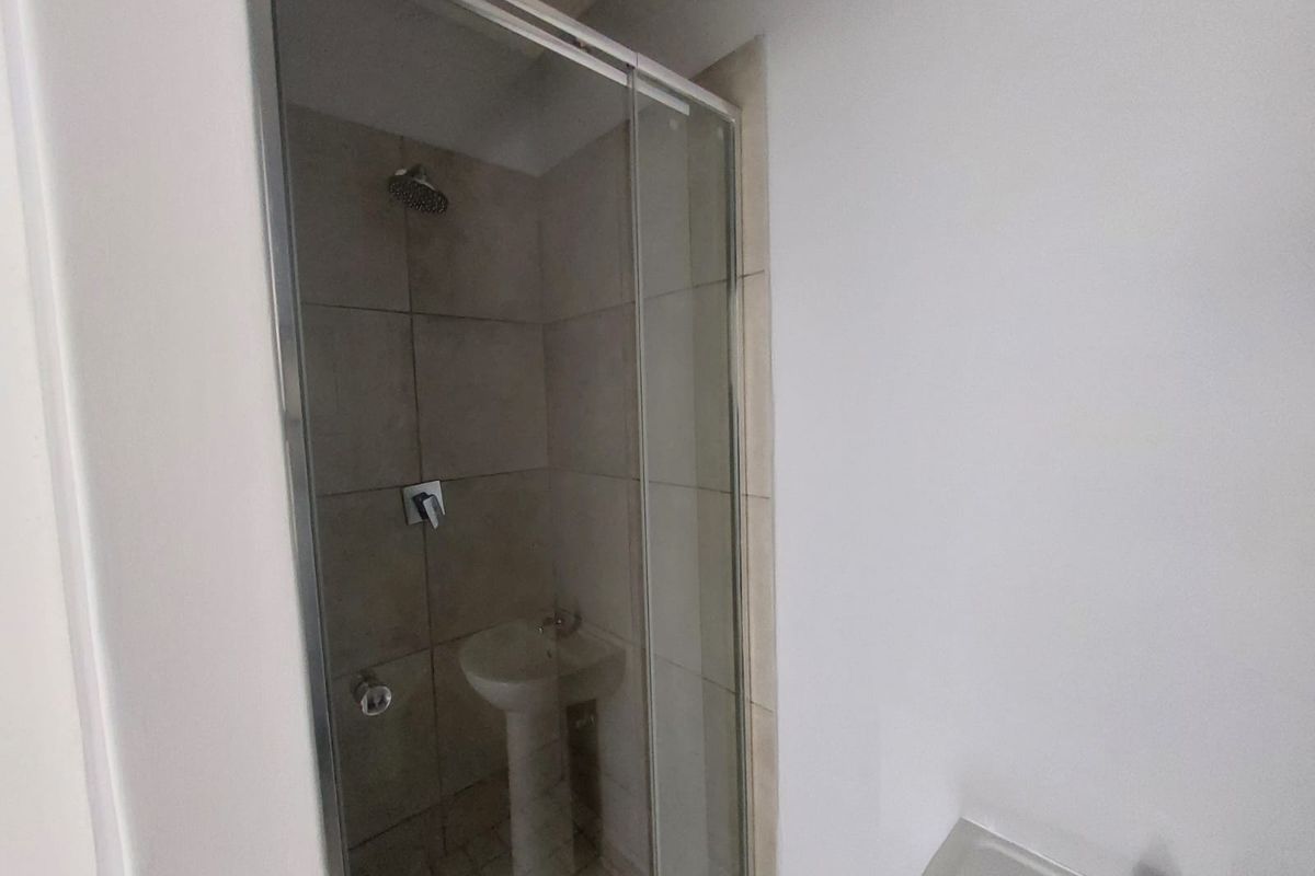 A functional bathroom featuring a tiled shower enclosure with a glass door and a pedestal basin.