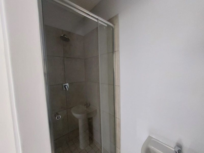 A functional bathroom featuring a tiled shower enclosure with a glass door and a pedestal basin.