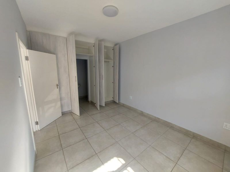 A clean, empty bedroom featuring neutral tiled flooring, light grey walls, and built-in storage cupboards with a modern finish.