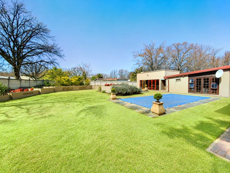 Spacious rear garden featuring a well-maintained lawn, a swimming pool with a cover, and paved areas adjacent to the house.