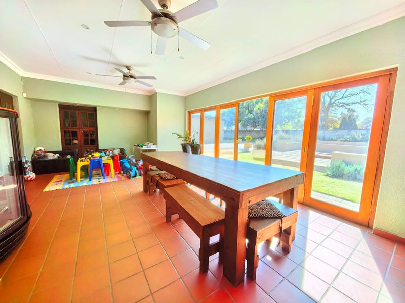 Spacious covered patio featuring terracotta tiled flooring, dual ceiling fans, and large wooden folding doors providing seamless access to the rear garden.