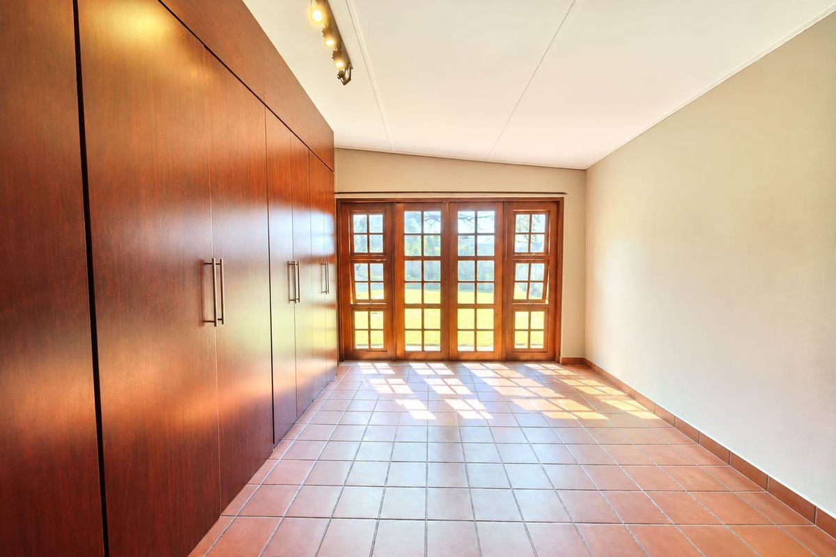 Spacious bedroom featuring extensive built-in wooden cabinetry, tiled flooring, and large wooden-framed glass doors providing natural light and garden access.