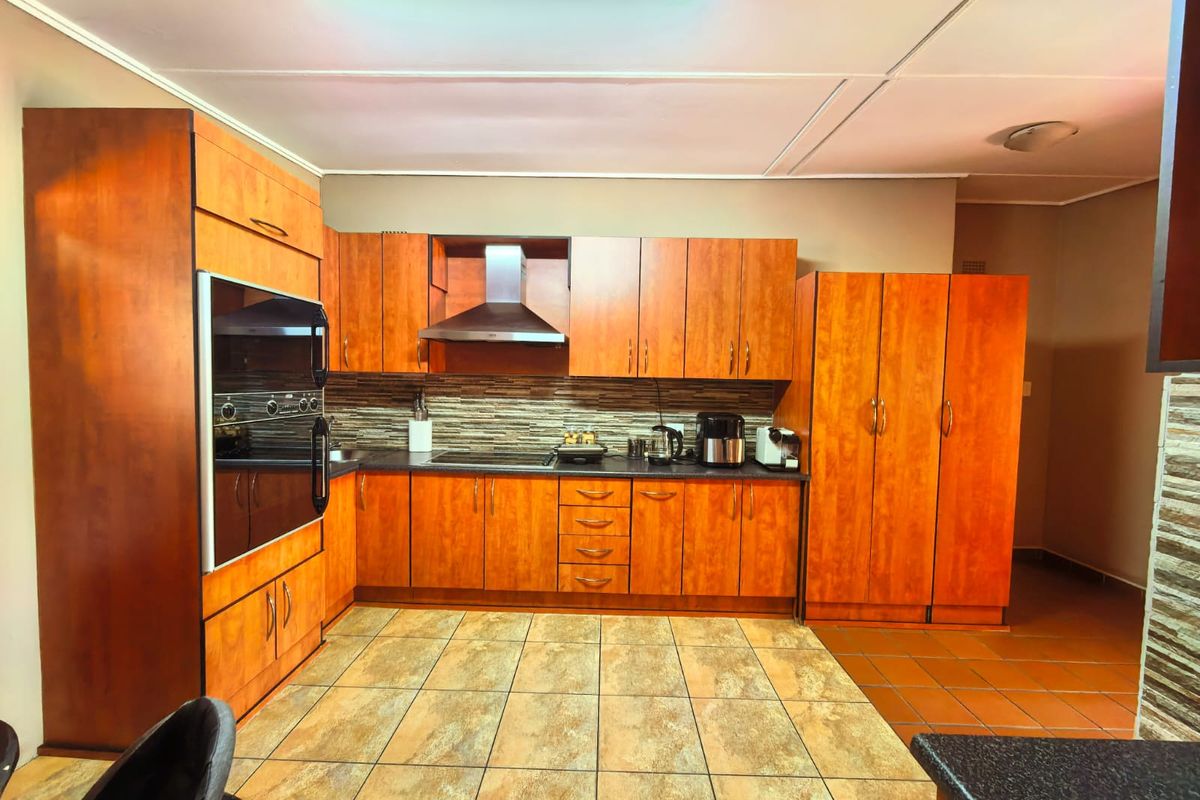 A functional kitchen featuring wood-finish cabinetry, built-in oven, extractor fan, and tiled flooring with a stone-look backsplash.