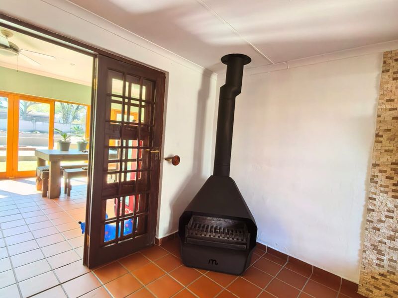 A bright living area featuring terracotta floor tiles, a modern freestanding fireplace, and a timber-framed glass door leading to an outdoor patio space.
