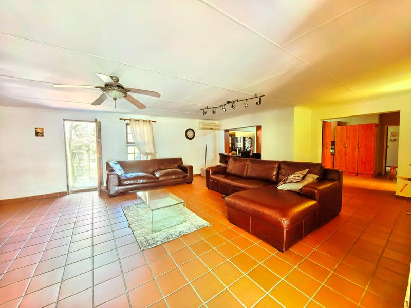 Spacious open-plan living area featuring tiled flooring, ceiling fan, track lighting, and a split-system air conditioner, with an adjacent kitchen area.