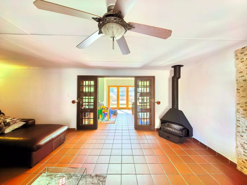 Living room featuring terracotta floor tiles, a freestanding fireplace, and french doors leading to an adjacent space with a stone feature wall.
