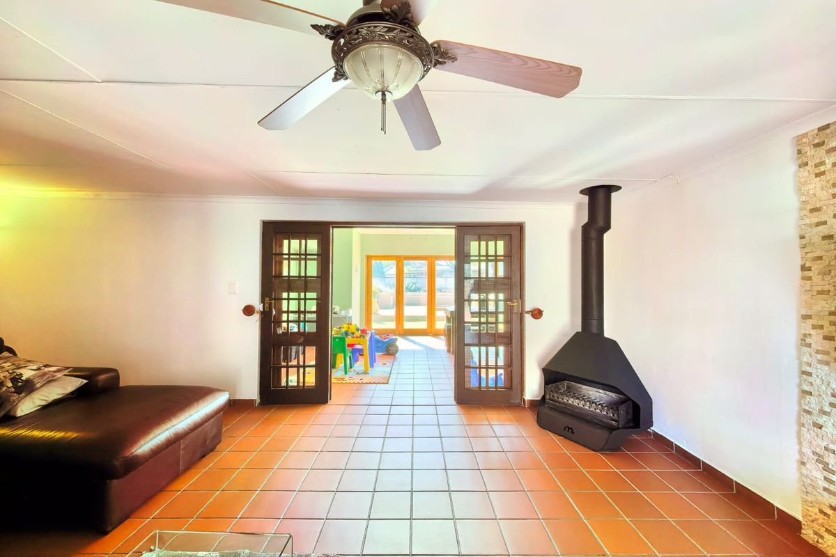 Living room featuring terracotta floor tiles, a freestanding fireplace, and french doors leading to an adjacent space with a stone feature wall.
