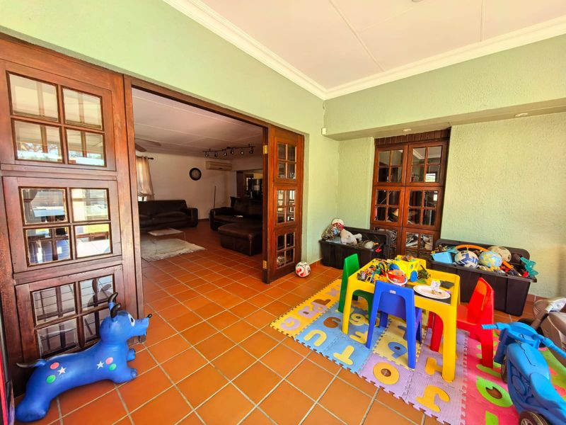 A covered patio area featuring terracotta floor tiles, wooden French doors leading to the living room, and a built-in wooden display cabinet.