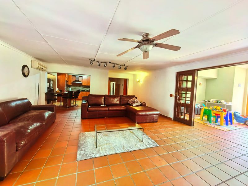 Spacious open-plan living area featuring terracotta floor tiles, a ceiling fan, and direct access to an adjoining kitchen and secondary room through french doors.
