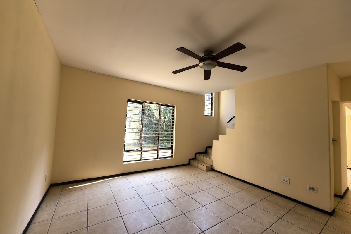 An empty living room featuring tiled flooring, a ceiling fan, and a staircase leading to the upper level.