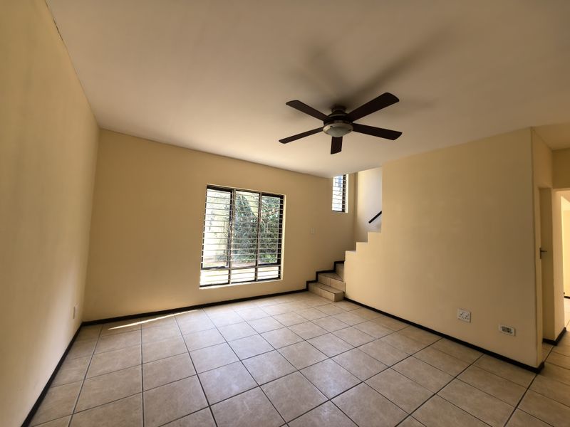 An empty living room featuring tiled flooring, a ceiling fan, and a staircase leading to the upper level.