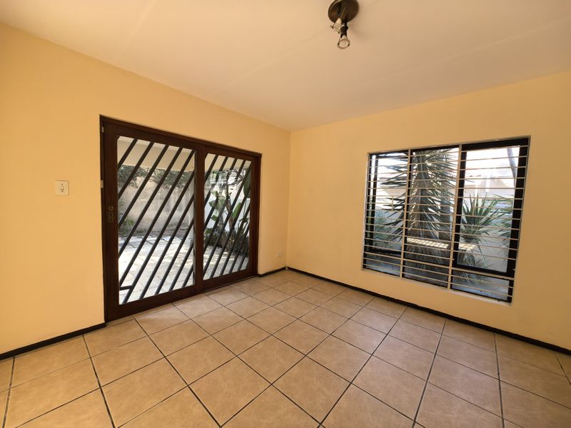 An empty living room featuring tiled flooring, a sliding glass door with security gate, and window security bars, offering direct access to the exterior.
