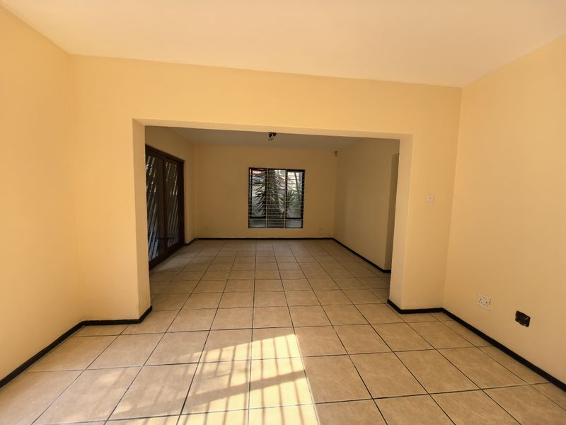 An empty, open-plan living area featuring neutral ceramic floor tiles, large windows with security bars, and a sliding glass door leading outdoors.