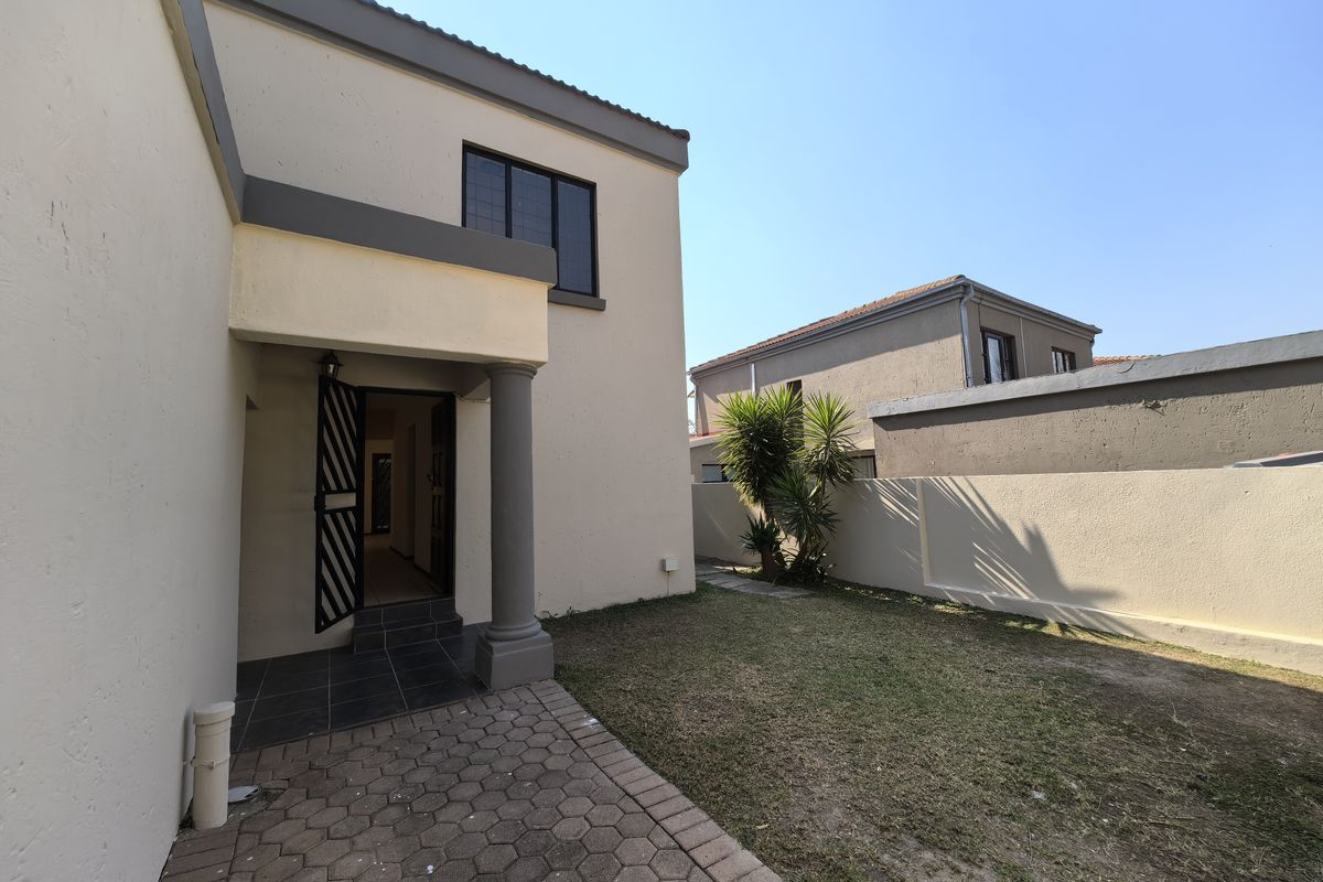 Rear exterior view featuring a paved patio area, a small garden space, and a secure entrance leading into the home.