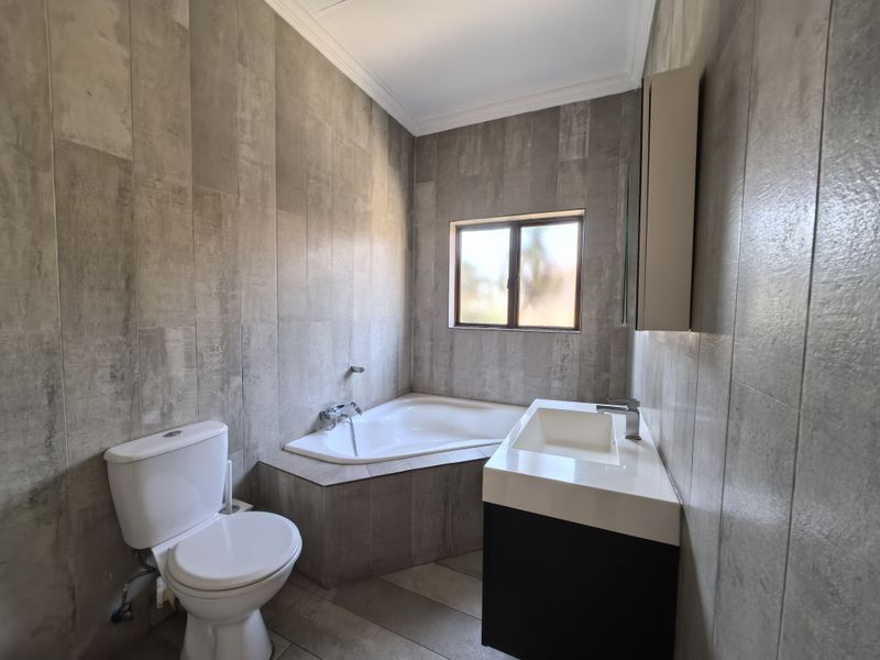 Modern bathroom featuring full-height wall tiling, a built-in corner bathtub, a contemporary vanity with basin, and a toilet.