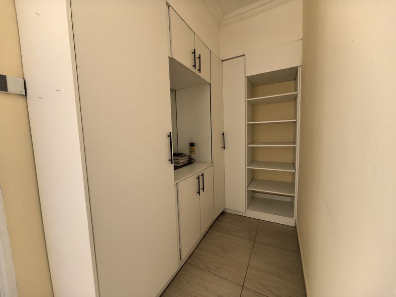 A functional bedroom area featuring extensive built-in white cabinetry with integrated shelving and durable tiled flooring.