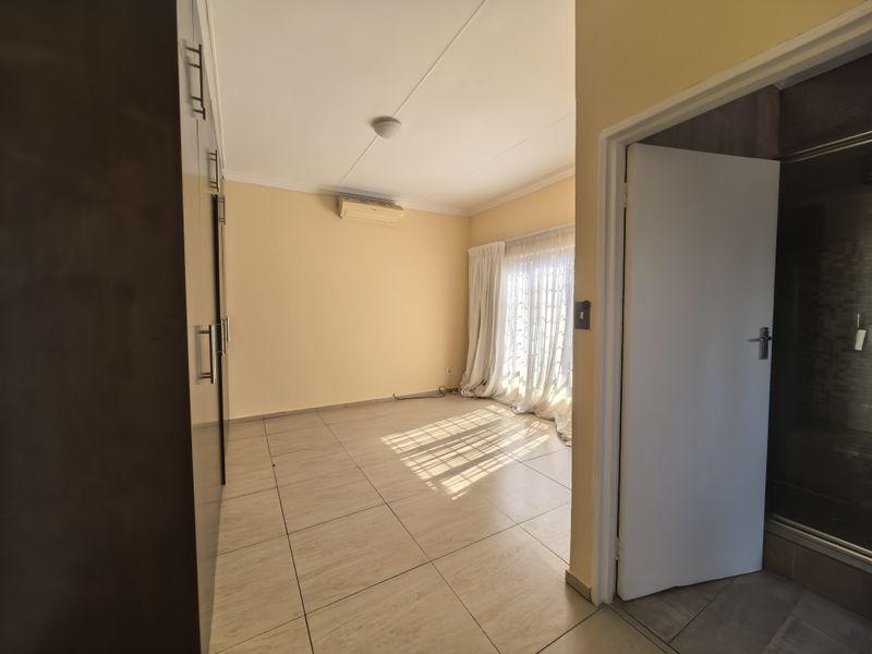 Spacious bedroom featuring tiled flooring, built-in cupboards, and an air conditioning unit, with direct access to an outdoor area through a sliding door.