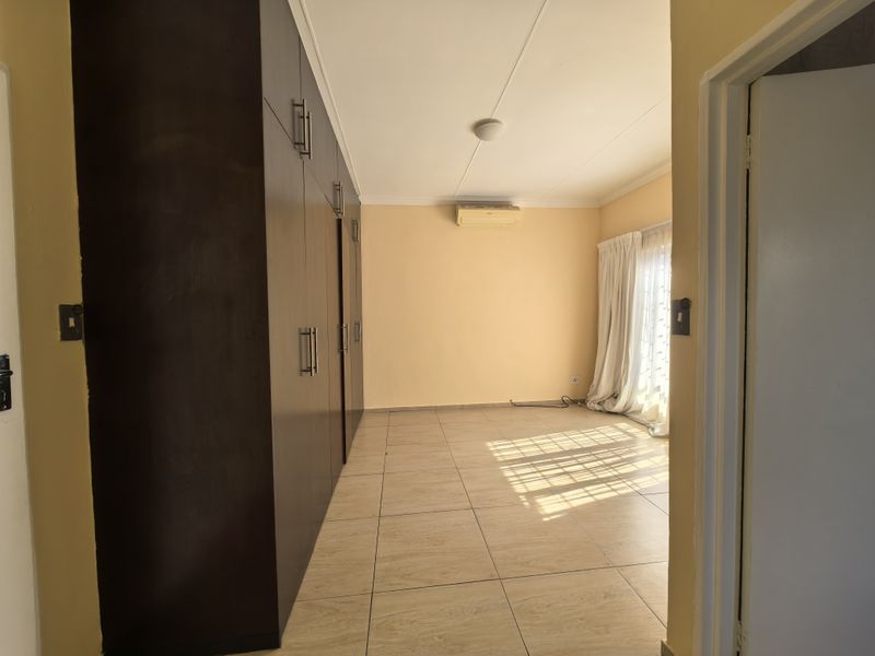 Spacious bedroom featuring built-in cupboards, tiled flooring, and a wall-mounted air conditioning unit, with access to natural light through a sliding door.