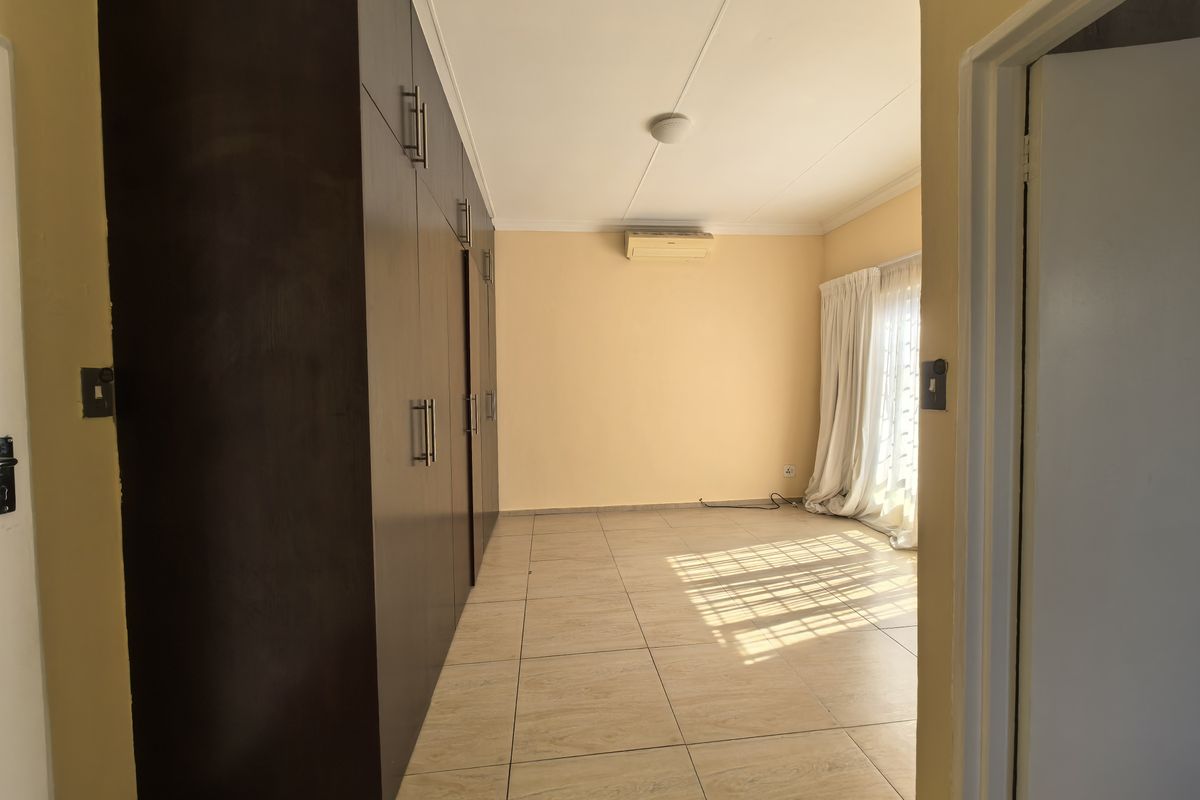 Spacious bedroom featuring built-in cupboards, tiled flooring, and a wall-mounted air conditioning unit, with access to natural light through a sliding door.