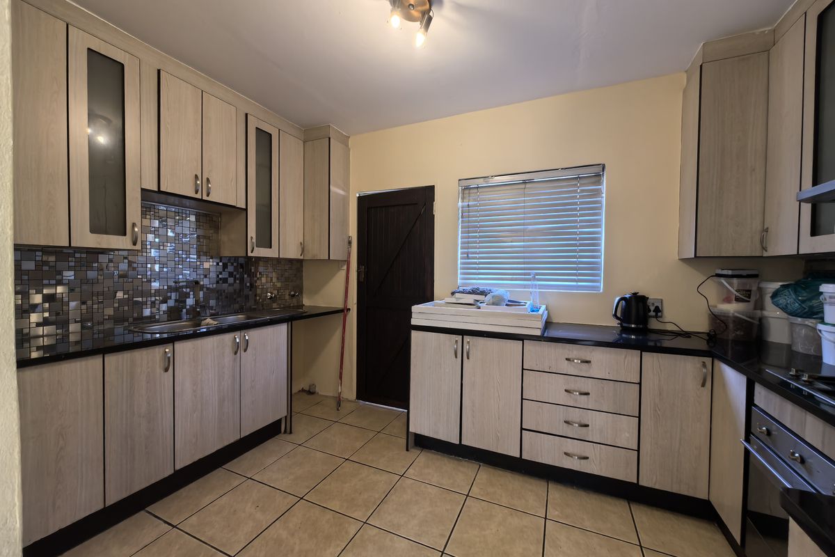 Functional kitchen featuring light wood-look cabinetry, mosaic tile backsplash, dark countertops, and ceramic floor tiles with direct access to an exterior door.