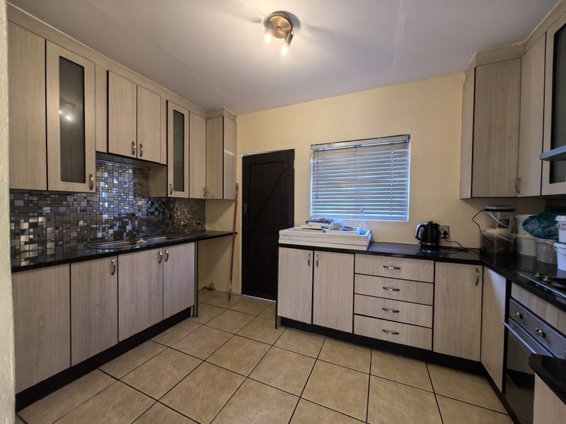Functional kitchen featuring light wood-look cabinetry, mosaic tile backsplash, dark countertops, and ceramic floor tiles with direct access to an exterior door.