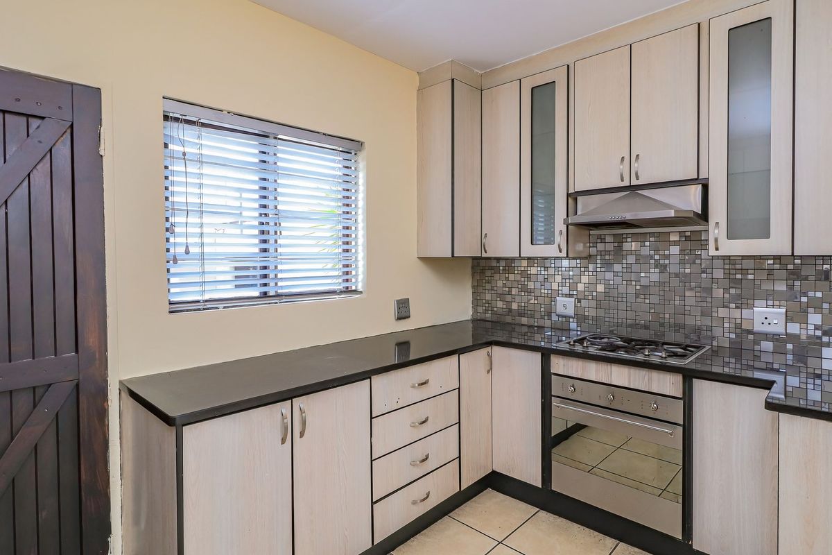 A functional kitchen featuring light wood-finish cabinetry, dark granite countertops, a mosaic tile backsplash, and integrated stainless steel cooking appliances.