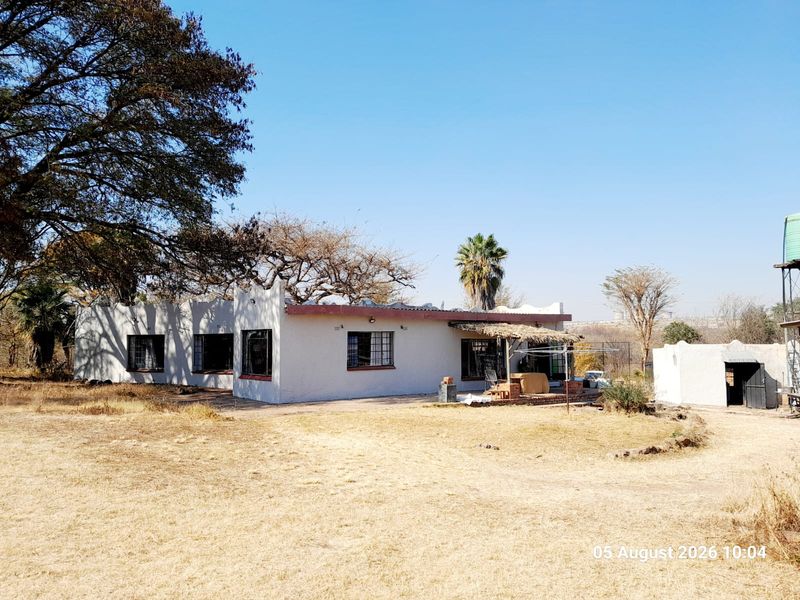 Rear view of a farm-style dwelling featuring security bars on windows, a small thatched patio area, and an adjacent water tank structure.